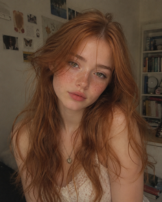 Woman with red hair and freckles wearing a lace top indoors