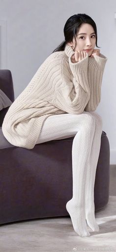 Woman in a cream turtleneck sweater and white tights sitting indoors