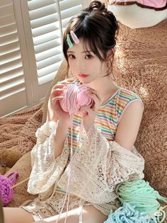 Woman holding pink knitting yarn, wearing a striped top and lace sleeves