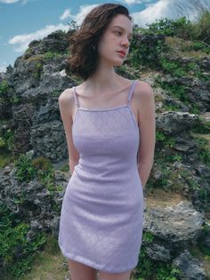Woman in a lavender dress standing outdoors against a rocky background