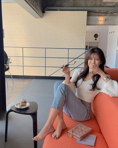 Woman in a white top and jeans sitting on an orange couch in a cafe