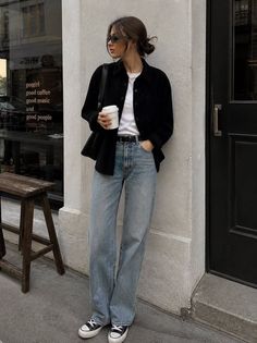 Woman in loose jeans and a black shirt holding a coffee cup on a street