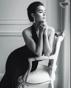 Woman in an elegant black dress and pearl earrings leaning on a classic chair