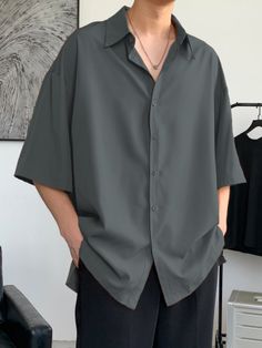 Person wearing a dark grey oversized short-sleeve shirt and black pants indoors