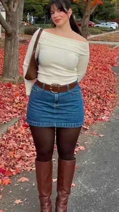 Woman in a denim skirt and off-shoulder top standing outdoors with autumn leaves