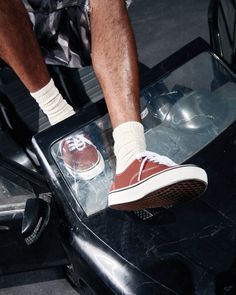 Person wearing red sneakers and white socks with camo shorts on a car window