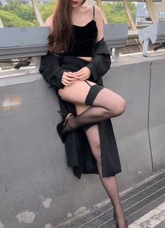 Woman in a black top, stockings, and high heels posing outdoors
