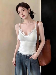 Woman in a white lace-trim camisole and denim jeans with a brown bag
