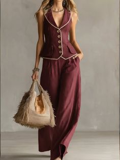 Woman in a maroon sleeveless top and wide leg pants holding a straw bag
