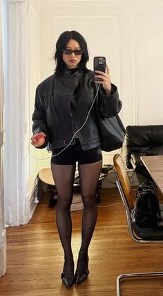 Woman in a black leather jacket, shorts, and tights holding an apple