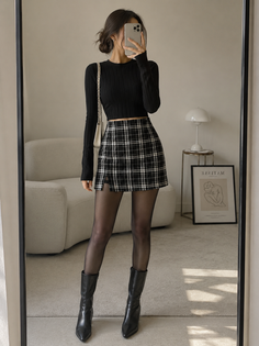 Woman in a black top and plaid skirt taking a mirror selfie