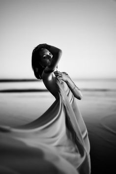 Woman with short hair and tattoos posing on a beach with flowing fabric