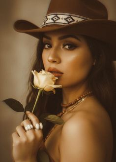 Woman in a cowboy hat holding a yellow rose to her lips