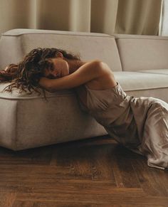 Woman with long curly hair lying on the floor next to a couch