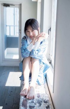 Woman in a plaid shirt sitting by a window with bare feet