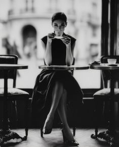 Woman in an elegant dress sitting at a cafe table, holding a coffee cup