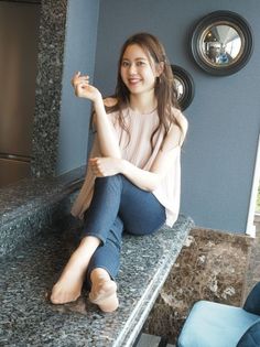Woman with long hair wearing jeans and a sleeveless top, sitting indoors