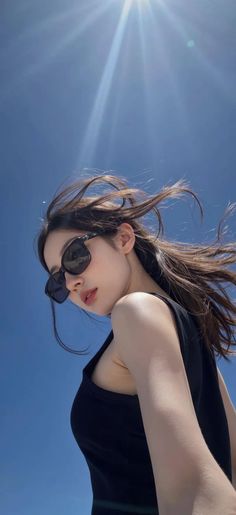 Woman in sunglasses with windblown hair against a clear blue sky