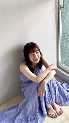 Woman in a purple dress sitting on the floor, laughing with bare feet