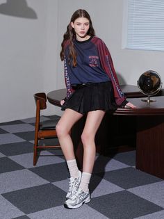 Woman in a long sleeve shirt and pleated skirt leaning on a desk