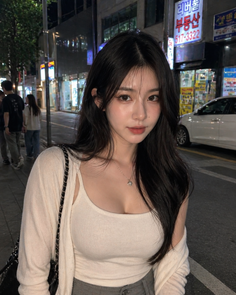 Woman with long dark hair wearing a white top and cardigan on a city street at night