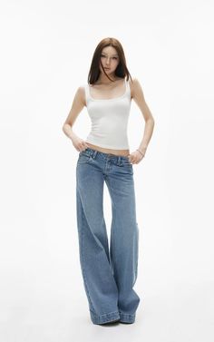 Woman in a white tank top and wide leg jeans posing in a studio