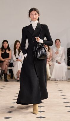 Model in a long black coat and white turtleneck on a runway