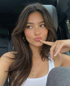 Woman with long brown hair and freckles wearing a white tank top and gold jewelry