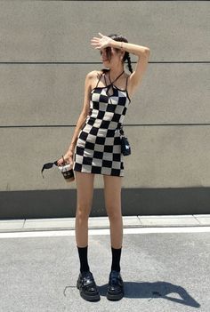 Woman in a black and white checkered dress shielding her eyes from the sun