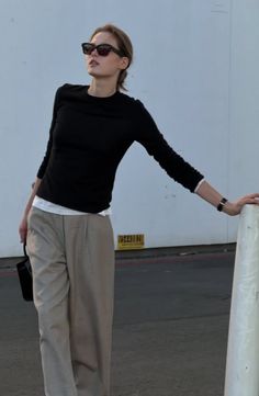 Woman in sunglasses, black long sleeve shirt, and wide leg pants outdoors