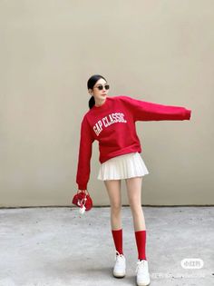 Woman in a red sweatshirt and white pleated skirt posing outdoors