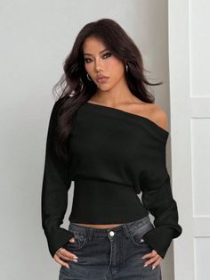Woman with long dark hair wearing an off-shoulder black top and dark jeans