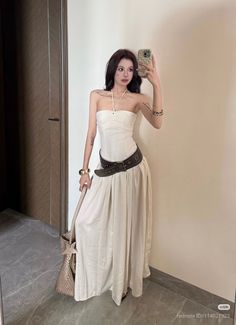 Woman in a white dress and dark belt taking a mirror selfie indoors