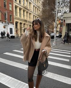 Woman in a beige coat and black shorts standing on a city street
