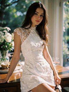 Woman in a white dress with lace and cherry details, leaning on a table indoors