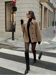 Woman in a camel coat and black dress crossing a street