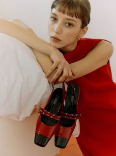 Woman in a red dress with short bangs holding red shoes