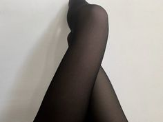 Person wearing black tights with legs crossed against a white background