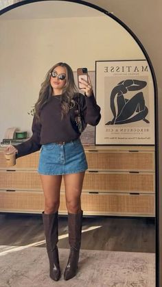 Woman in a denim skirt and knee-high boots taking a mirror selfie indoors