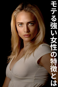 Woman with blonde hair and green eyes in a white dress against a dark background