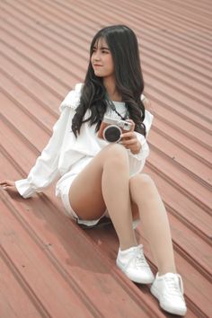 Young woman with long dark hair sitting outdoors, holding a camera