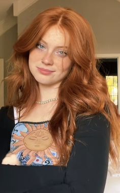 Young woman with long red hair and blue eyes wearing a sun graphic top and pearl necklace