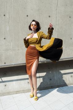Woman in a crop top and high-slit midi skirt with a long jacket and sunglasses