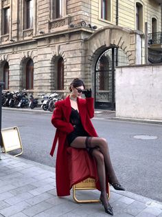 Woman in a red coat and black lingerie with stockings sitting on a chair outdoors