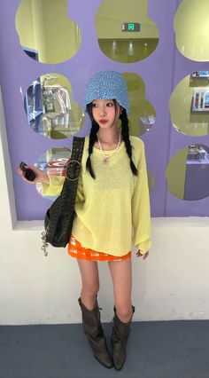 Woman in a blue hat, yellow sweater, and orange skirt with braids and cowboy boots