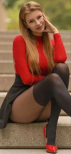 Woman with long hair in a red top and black skirt sitting outdoors