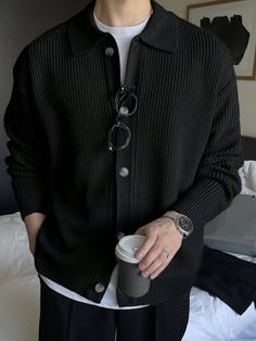 Person wearing a black cardigan over a white t-shirt, holding a coffee cup