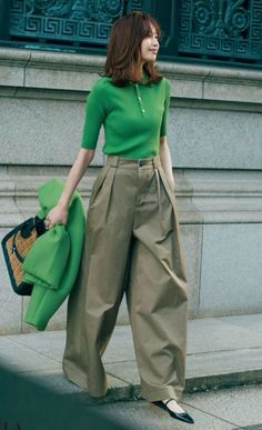 Woman in a green polo shirt and wide leg pants holding a wicker bag outdoors