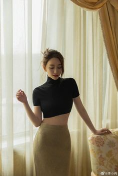 Woman in a black crop top and olive midi skirt indoors with soft lighting