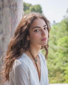 Woman with long wavy hair and freckles wearing a white shirt and bolo tie outdoors